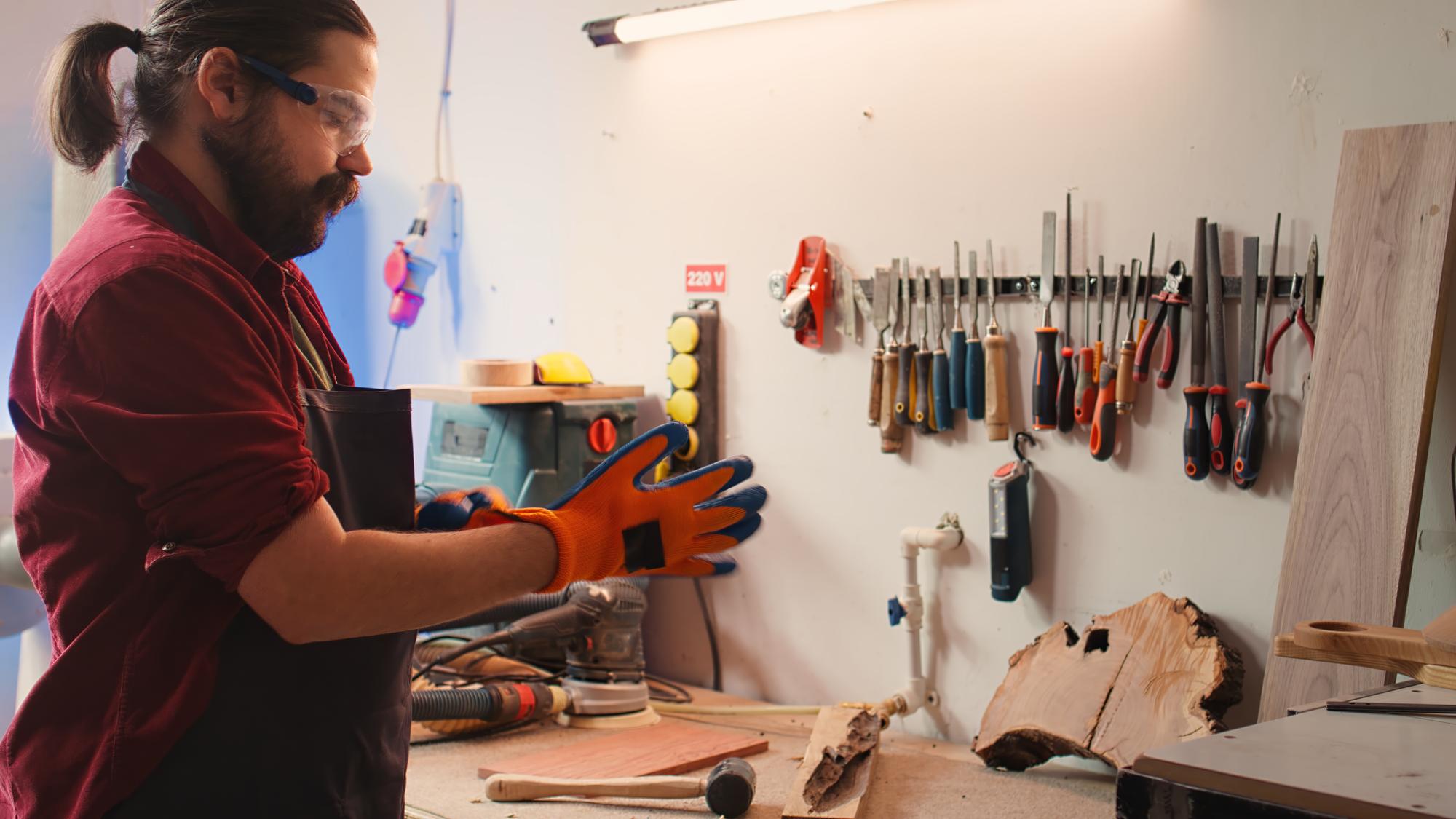 Artisan menuisier travaillant le bois dans son atelier, équipé de gants de protection