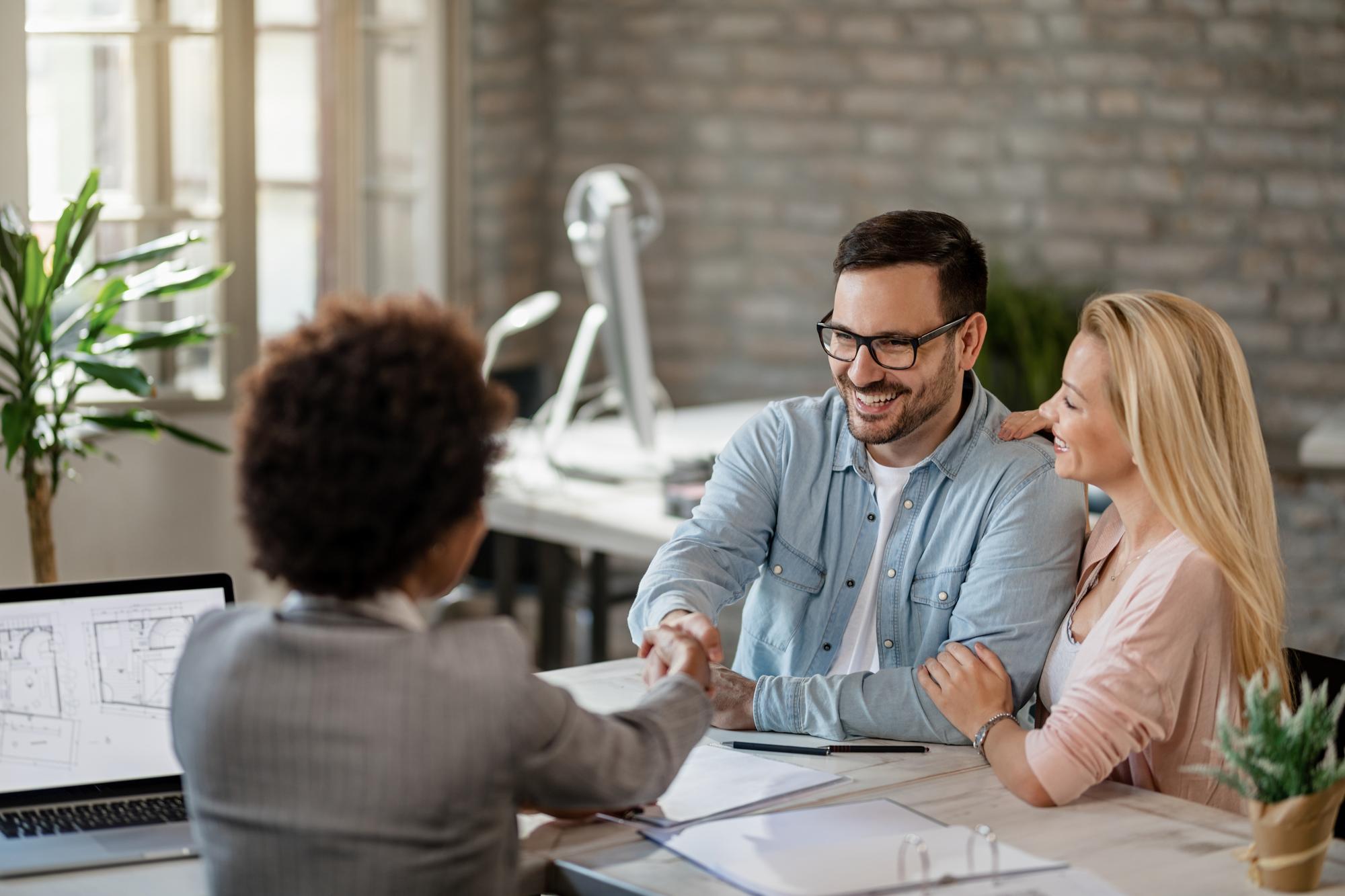 Agent immobilier en rendez-vous avec des clients, dossier et plan sur ordinateur portable
